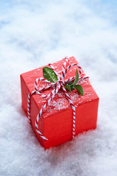 Red Christmas Gift Box with Boxwood Leaves and Candy Cane Ribbon on Surface of Snow