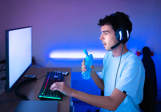 Man playing online  games on his computer and drinking water from a bottle
