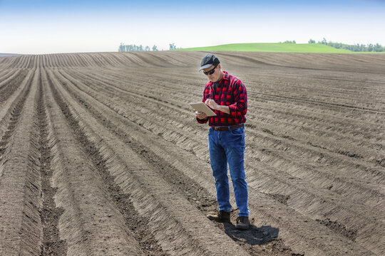 A farmer stands using a tablet on freshly tilled farmland; Alberta, Canada
