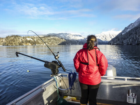 Rear view of woman standing in boat next to outrigger with fishing rods and looking at the mountains near Homer; Alaska, United States of America