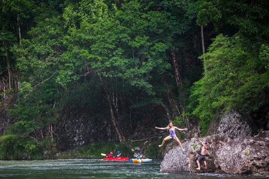 A woman jumps off of a rock and into the water in the Tully Gorge National Park; Queensland, Australia