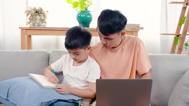 4K, An Asian single father is sitting with his son on sofa in living room of house, son was sitting and painting picture drawn from his imagination, and father was working in his own notebook.