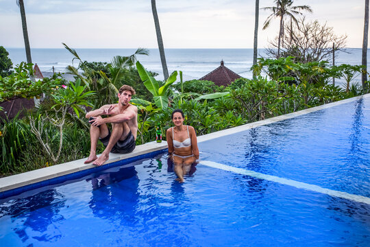 Man and woman sitting poolside at resort, overlooking surfing beach of Balian Beach; Selemadeg Barat, Tabanan, Bali, Indonesia