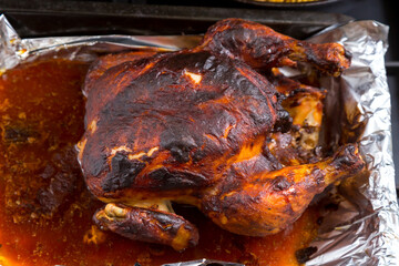 Chicken baked whole in sauce on foil close-up.