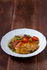 Pasta with vegetables and baked chicken leg with tomatoes sprinkled with green onions in a plate on a wooden table.copy space