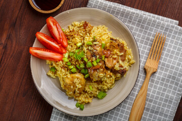 Thai chicken rice garnished with green onions on a wooden table next to soy sauce napkin and wooden fork.copy space
