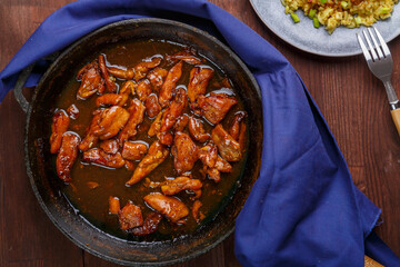 Fried chicken pieces in soy and pad thai sauce in a pan on a blue napkin on a laid table.