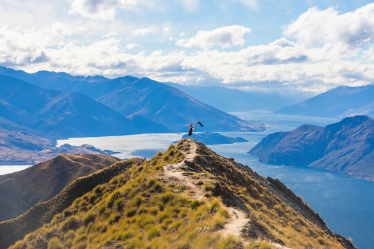 Man standing on mountaintop at Roys Peak waving the New Zealand flag
