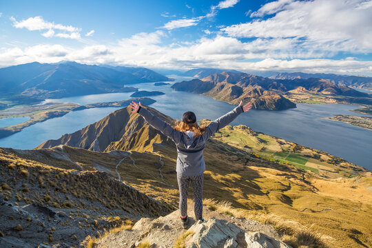 The strenuous yet highly rewarding hike to Roys Peak in Wanaka. The hike is difficult but the views are spectacular. A traveler celebrates at the summit; Wanaka, Otago, New Zealand