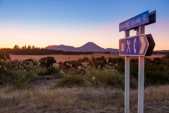 A beautiful sunset in the Tongariro National Park. The volcanic Mount Doom (Mount Ngauruhoe) can be seen in the background, with a roadside sign in the foreground; Manawatu-Wanganui, New Zealand