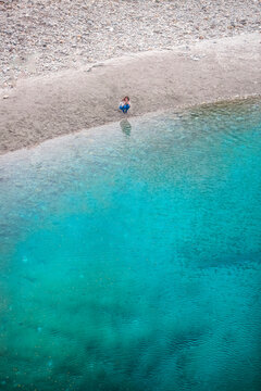 The Blue Pools of Makarora offer enticing blue waters to swim in. A woman crouches by the water's edge to take a picture with her camera, Mount Aspiring National Park; Makarora, Otago, New Zealand
