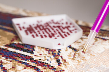 A stylus with a red acrylic rhinestone on the tip, close-up over a fragment of a diamond mosaic....