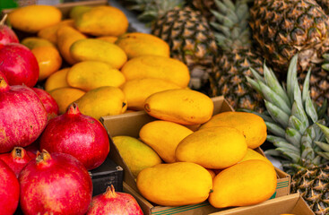 close up of mangoes, pineapples and pomegranates on counter in store. textured background of natural fruits