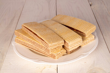 Several sweet chocolate wafers with a white plate on a wooden table, close-up.