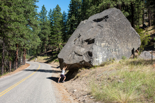 Woman pretending to push large boulder uphill, Eastern Washington, Sinlahekin Wildlife Area, WA, USA