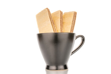 Three sweet chocolate wafers in a black ceramic cup, close-up, isolated on a white background.