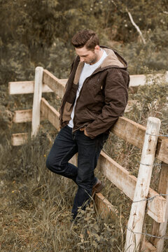 A young man stands against a rail fence looking serious and contemplative; Alberta, Canada
