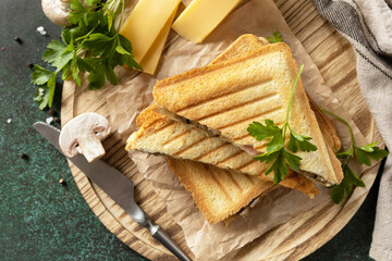 Delicious sandwich with grilled cheese, bacon and mushroom. Homemade breakfast on a dark stone tabletop. View from above.