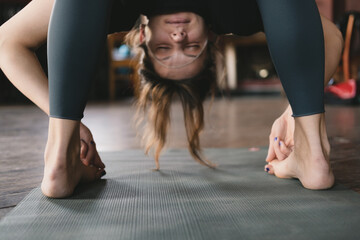 Close-up photo of a new yoga teacher woman in standing forward fold pose variation hooking big toes (Padangusthasana) in her vinyasa flow yoga practice