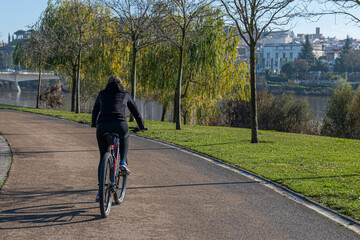 Unrecognizable Person Enjoying Daily Exercise Routine. Rear View Of A Young Woman Riding A Bicycle In The Park In The City. Young Person Keeping Fit, Healthy Lifestyle. Sports.