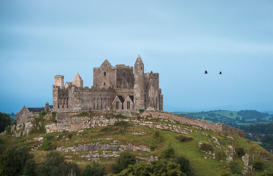 The ancient Rock of Cashel on the hilltop with two birds flying against the cloudy sky; Cashel, County Tipperary, Ireland