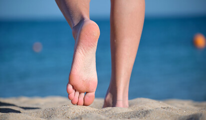 Close up of female feet walking barefoot on white grainy sand of golden beach on blue ocean water...