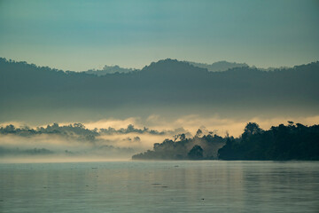 Dawn, with sunlit morning mist rising over the jungle covered banks of the Ayeyarwady (Irrawaddy) River at dawn; Rural Jungle, Kachin, Myanmar (Burma)
