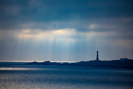 Hellisoy Lighthouse, a remote lighthouse on an island in the Western Fjords of Norway with sun rays reflecting through a stormy sky; Hordaland, Norway