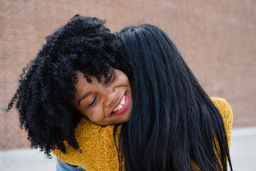 Interracial couple happily embracing in the suburbs with a brick background.