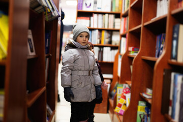 Fototapeta na wymiar Little cute sisters in jacket reaching a book from bookshelf at the library. Learning and education of european girl kid.