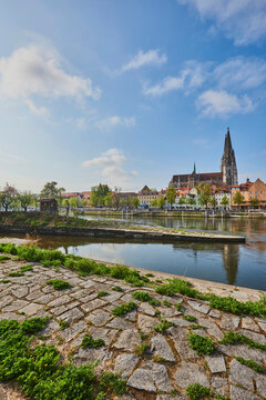 Outlook over the Danube River with the old, Gothic St Peter's Cathedral from the stone path on Marc​-Aurel-shore in the Old Town of Regensburg with a blue sky at sunset; Regensburg, Bavaria, Germany