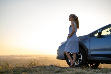 Young female driver resting near her car enjoying warm summer evening. Travel and getaway concept