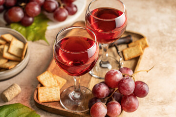Two glasses of red wine, a bunch of red grapes, crackers and corkscrew on a wooden tray on beige textured background with text space. Party for two concept