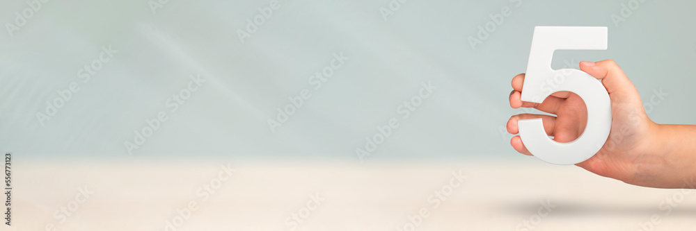Aufkleber Number five in hand. Hand holding white number 5 on blurred background with copy space. Concept with number five. Birthday 5 years, fifth grade, five day work week
