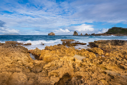 Waves crashing along the rock formations along the shore at Grande-Terre with the Grand-Croix in the distance at the top of Pointe des Chateaux; Guadeloupe, French West Indies