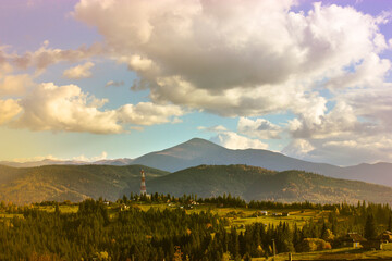 Fototapeta premium Beautiful mountain scenery with blue sky, white low clouds in a sky at sunny day in spring, summer or fall. A mountain top on a horizon and green coniferous forest. Ukrainian Carpathians landscape.