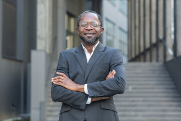 Successful african american boss with arms crossed smiling and looking at camera mature man outside office building.