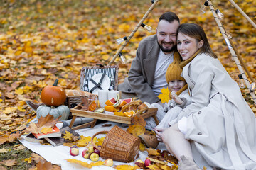 Happy family on a beautiful fall picnic in the park. Cozy autumn vibes. Young father, mother and their cute son spending quality time together, having fun in the park
