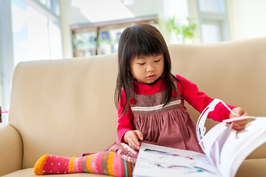 Young girl sits on a couch reading a storybook; Hong Kong, China