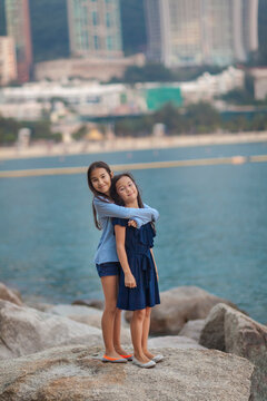 Young sisters stand in an embrace on boulders at Repulse Bay in Hong Kong; Hong Kong, China