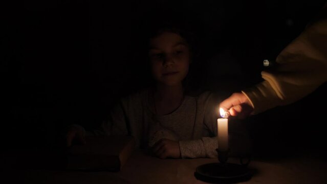a girl is lit a candle so that the child can read a book
