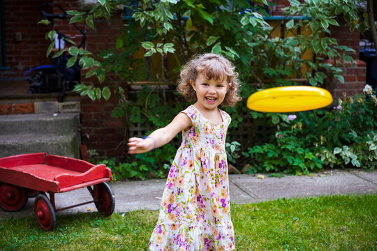 Preschooler girl throwing a frisbee towards the camera in her yard at home; Toronto, Ontario, Canada