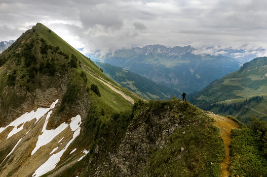 A hiker reaching a mountaintop and looking out at the magnificent vista of the alps with a cloudy sky; Feldkirch, Vorarlberg, Austria