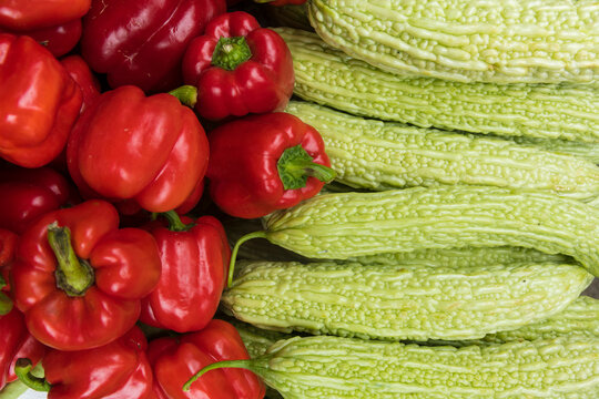 Close-up detail of a pile of red peppers (Capsicum annuum) and rows of bitter melons (Momordica charantia) for sale in Chengdu Market; Sichuan, China
