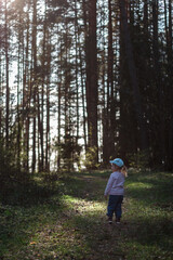 Obraz premium A three-year-old girl walks through a pine forest in the spring on a sunny day. Vertical orientation.