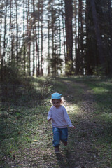 A three-year-old girl runs through a pine forest in the spring on a sunny day. Vertical orientation.