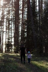 Obraz premium A three-year-old girl and her dad are walking in a pine forest in the spring on a sunny day.