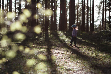 A girl of three years old stands in a pine forest in the spring on a sunny day.