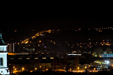 Fototapeta na wymiar Ostrowiec Świętokrzyski nocą . Widok miasta z góry . Zabudowania starej huty , światła miasta . Oświetlona droga wspinająca się na wzgórza .