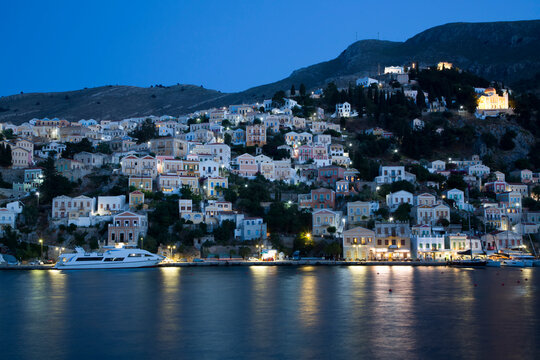 Illuminated buildings on the waterfront in the evening at Gialos Harbor, Symi (Simi) Island; Dodecanese Island Group, Greece